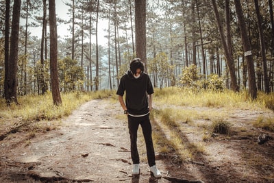 身穿黑色长袖衬衫和黑色裤子的男子站在树木环绕的土路上
